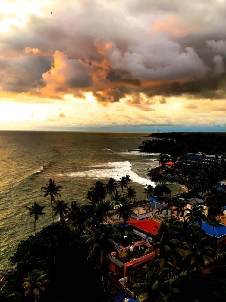 Storm clouds lit orange above a palm-lined coast seen from above.