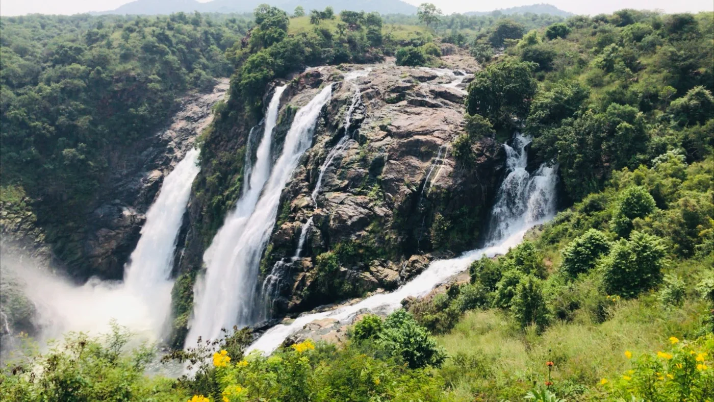 Waterfalls pouring down a rocky green hillside.