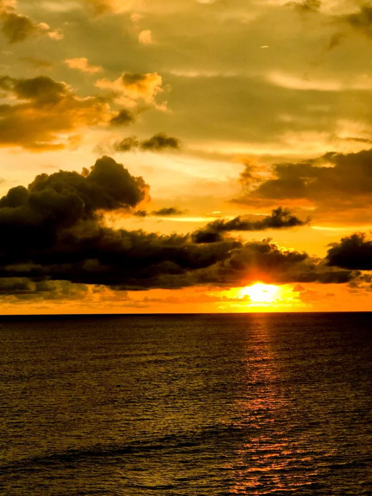 A golden sunset behind dark clouds over a calm sea.