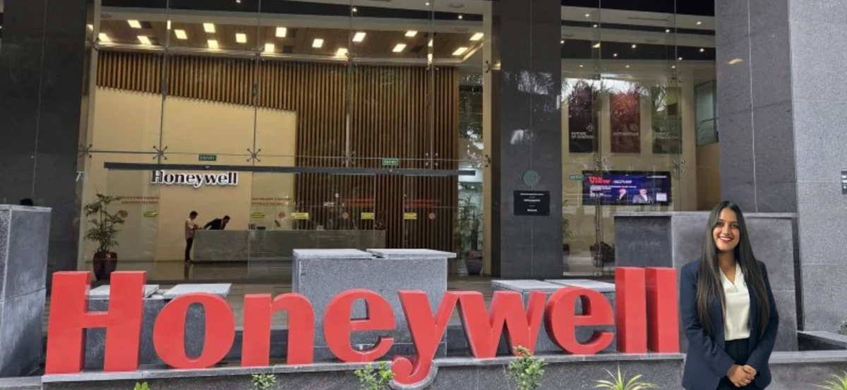 Vibha in a navy blazer standing beside the large red Honeywell sign outside the Honeywell office entrance.