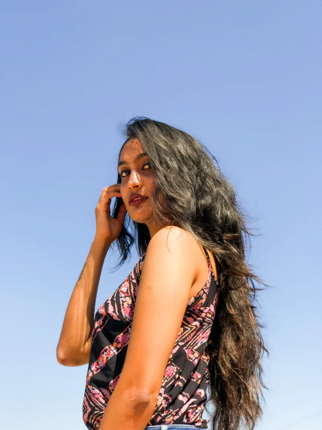 A woman with long windswept hair looking back at the camera against a clear blue sky.