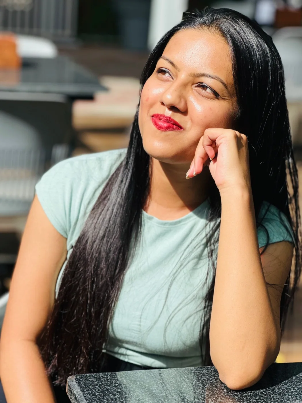 A woman in a mint T-shirt resting her chin on her hand, looking up and smiling in sunlight.