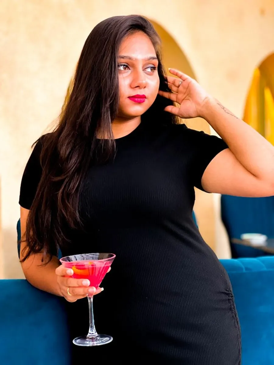 A woman in a black dress holding a pink cocktail, looking away.