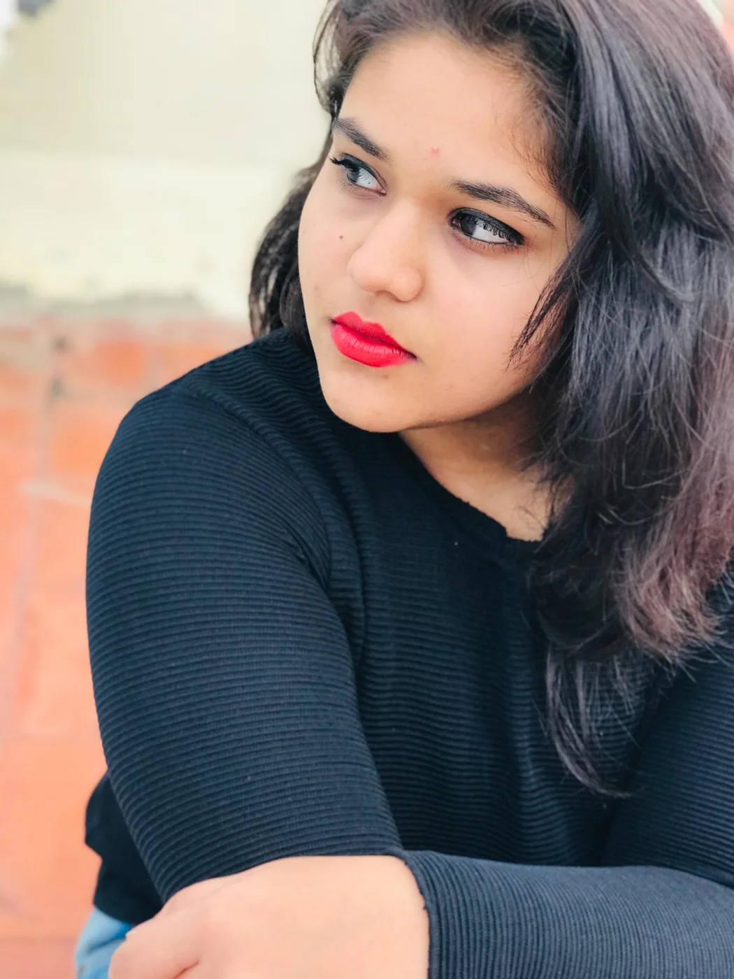Close portrait of a woman in a black jumper with red lipstick, looking off to the side.