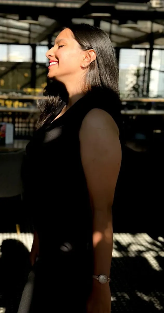 A woman in profile, eyes closed and smiling, with sun across her face.